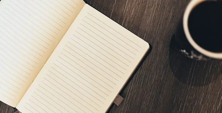 Blank notebook on a table next to a coffee mug