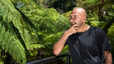 Bling presenter Amir Latif stood in front of lush green leaves on a brige looking into the distance
