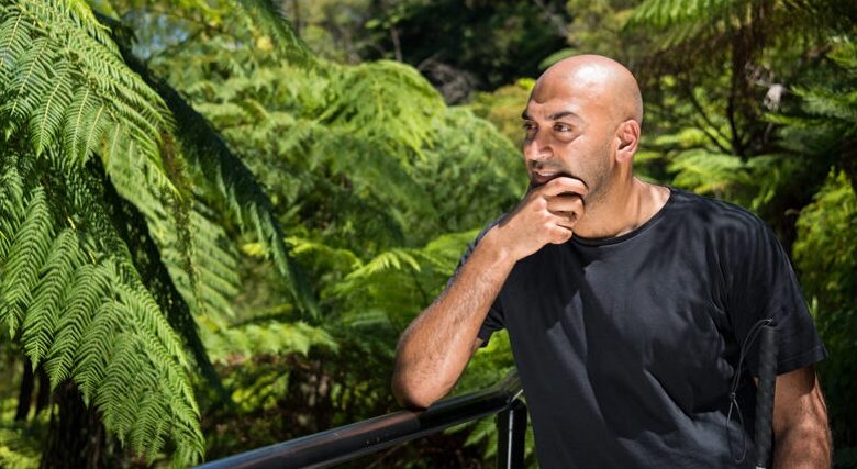 Bling presenter Amir Latif stood in front of lush green leaves on a brige looking into the distance