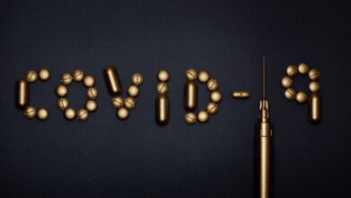 Covid-19 spelt out in gold tablets on a black background with the one a syringe and needle