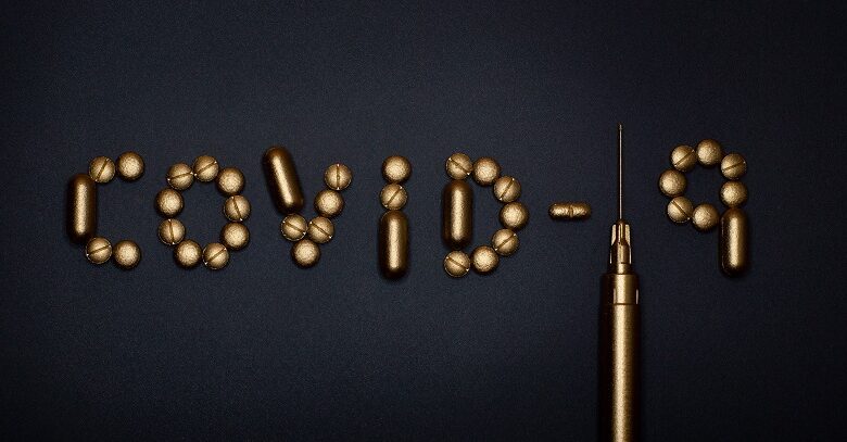 Covid-19 spelt out in gold tablets on a black background with the one a syringe and needle