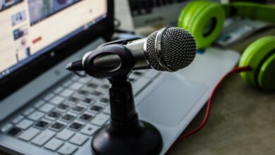 Microphone sat on a laptop with the screen open and a pair of green headphones
