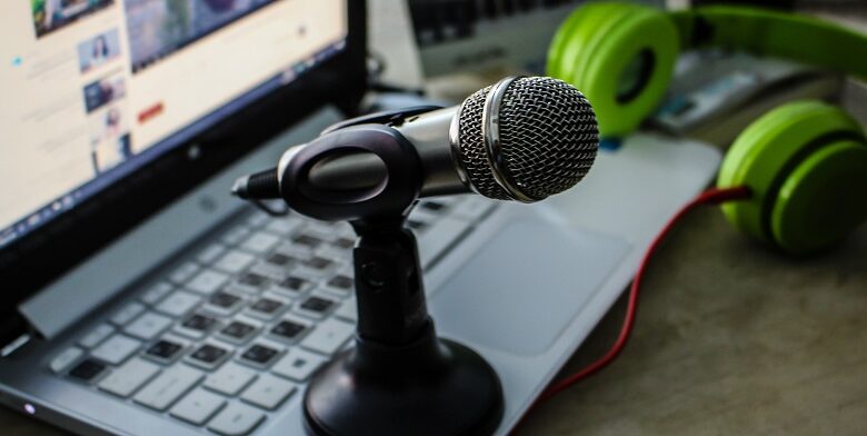 Microphone sat on a laptop with the screen open and a pair of green headphones