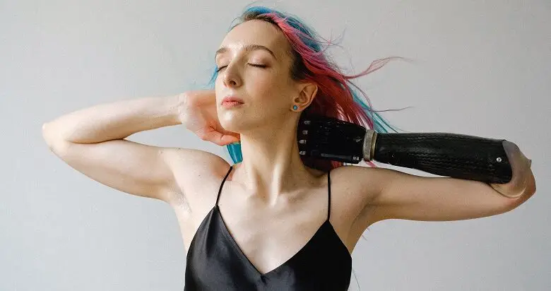 Woman wearing a black silk strap top with pink and blue hair and a prosthetic arm