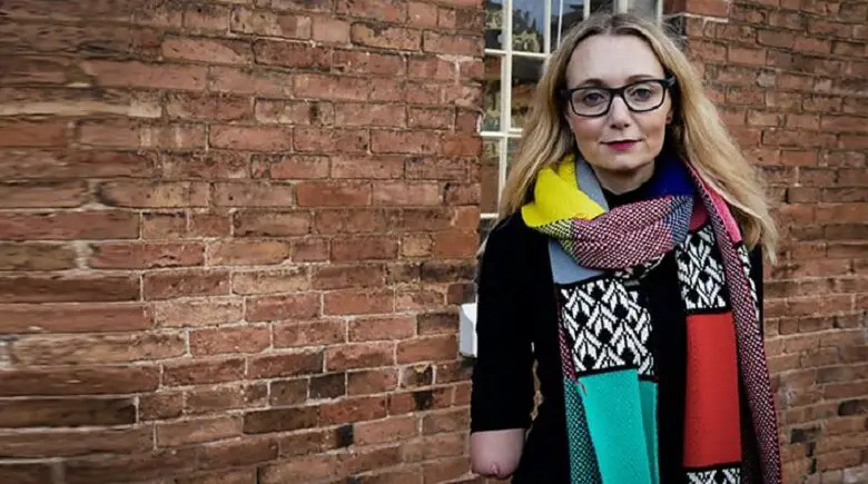 Carrie Brunell wearing a black top and colourful scarf stood in front of a brick wall