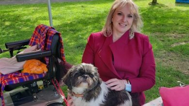 Emma Shepherd wearing a pink coat sat on a bench in a park with her dog on her lap and her mobility scooter behind her