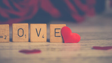 Love spelt with Scrabble letters. Roses positioned behind them - by Nietjuh