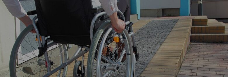 Wheelchair user going up a paved ramp in a manual chair being viewed from behind