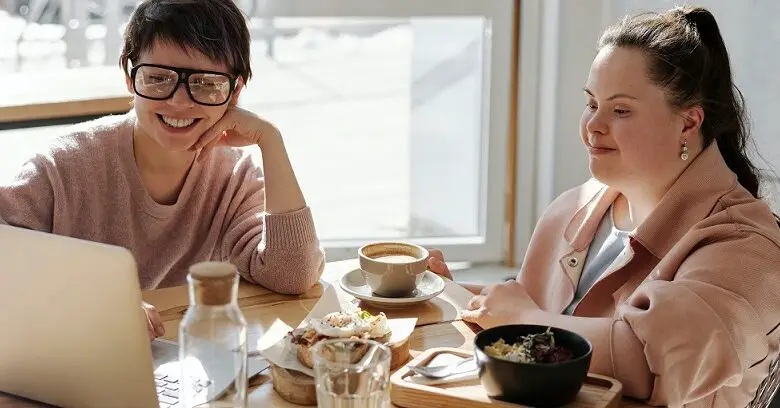 Woman with Down's Syndrome sat at a table with another woman using a laptop