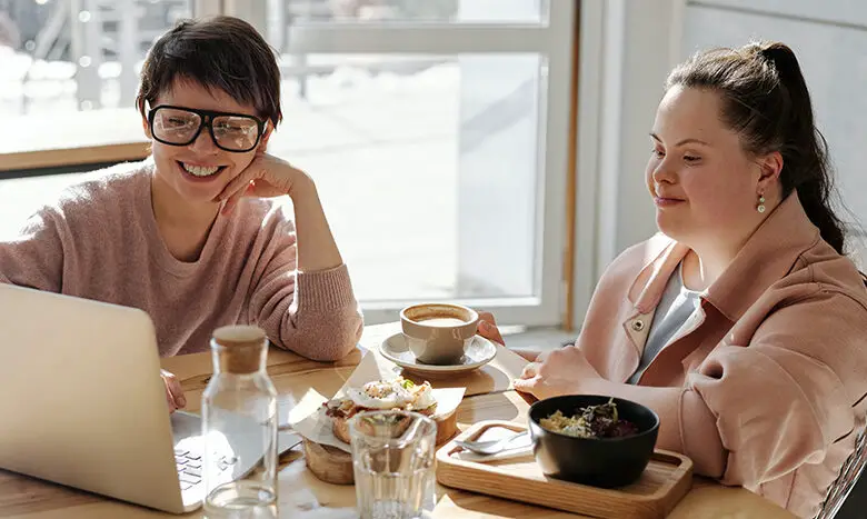 Lady with down syndrome is working with a colleague on a laptop - by Cliff Booth