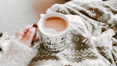 Mug of tea on a woman's lap covered in a grey fleece blanket