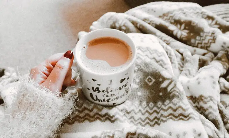 Mug of tea on a woman's lap covered in a grey fleece blanket