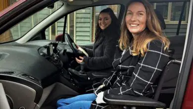 Two woman sat in an adapted car with the wheelchair user as a passenger upfront next to the driver