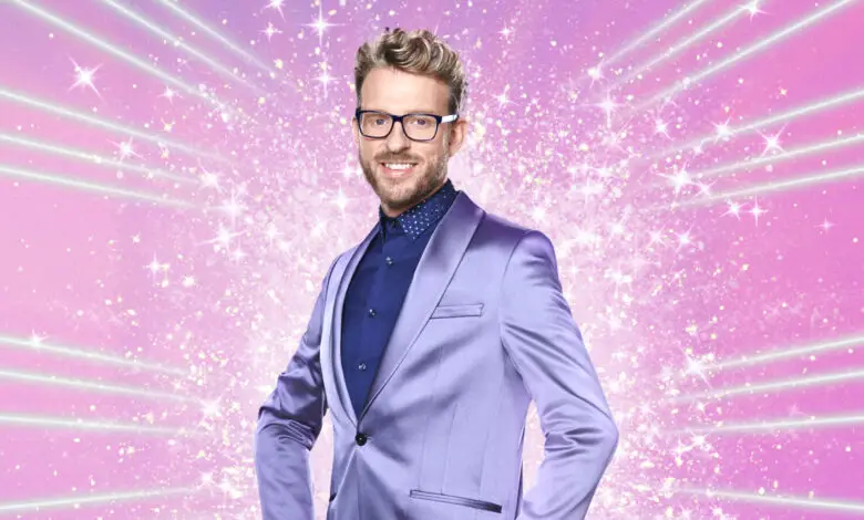 JJ Chalmers in a lilac suit and blue shirt stood in front of a pink, sparkly background