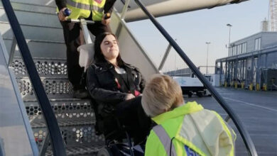 A lady is being transfered in her wheelchair inside of an airplane