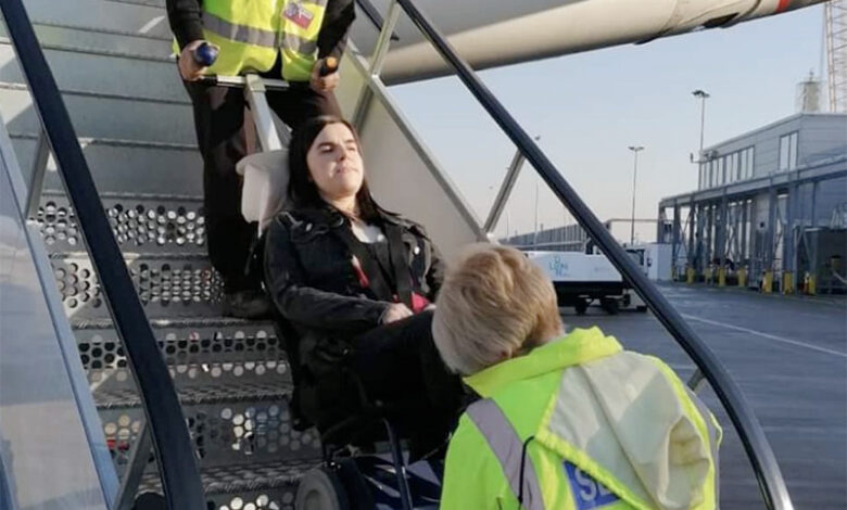 A lady is being transfered in her wheelchair inside of an airplane
