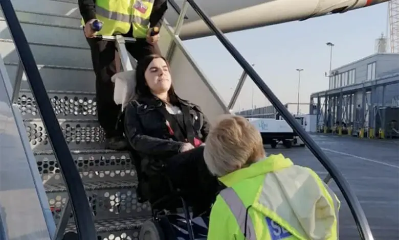 A lady is being transfered in her wheelchair inside of an airplane