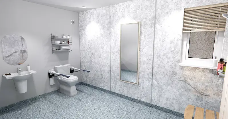 Accessible bathroom in an adapted modular home extension with grey floor and wall tiles, a toilet with supports, walk-in shower and shower chair