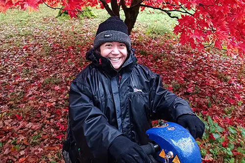 Emma is sitting on her scooter under a beautiful red tree - Photo by Emma West
