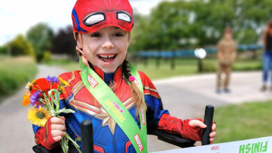 A young girl is dressed in a superhero costume and is crossing a finish line