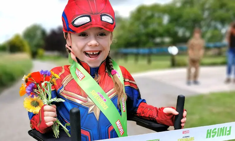 A young girl is dressed in a superhero costume and is crossing a finish line