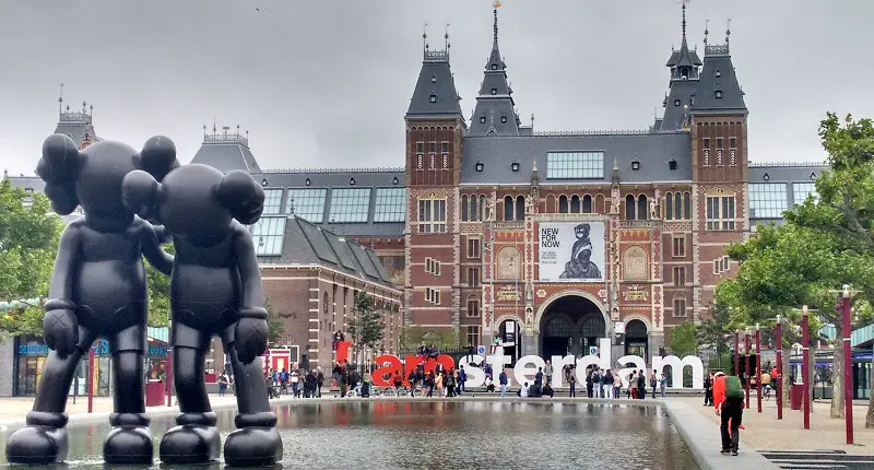 Accessible Rijksmuseum Amsterdam, Netherlands seen from the front with two modern black statues in front of two people