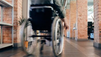 Close up of the back of a wheelchair being wheeled by a man through an office