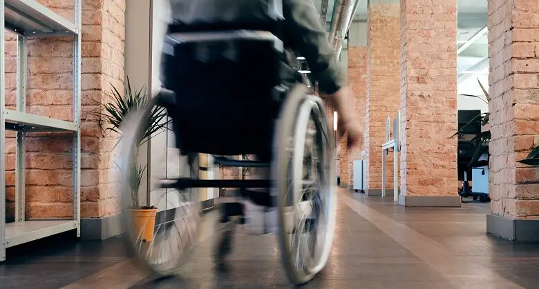 Close up of the back of a wheelchair being wheeled by a man through an office