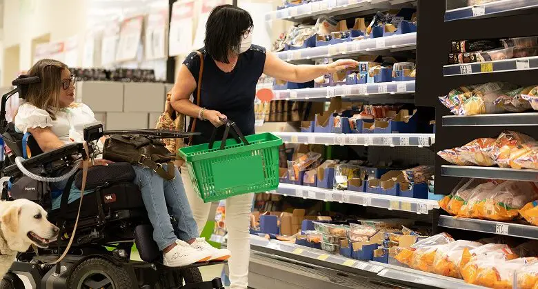 Hannah in her powerchair with her carer and assistance dog in a supermarket