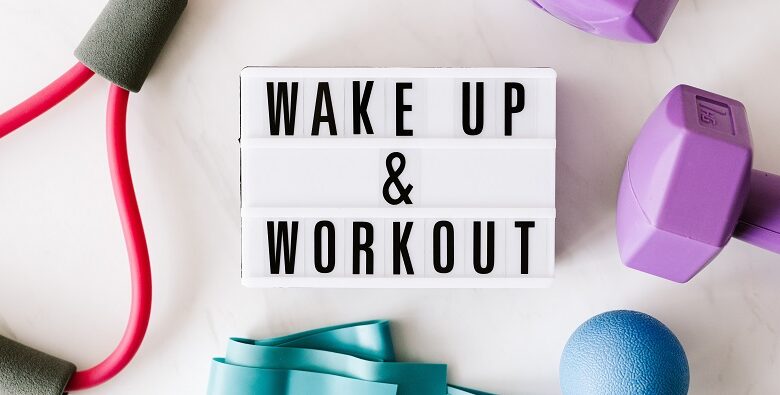 Wake up and work out sign surrounded by purple weights, a turquise elastic band and arm exerciser