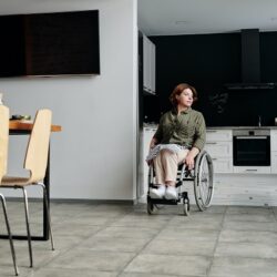Woman using a wheelchair wheeling out from her open-plan kitchen into her dining room