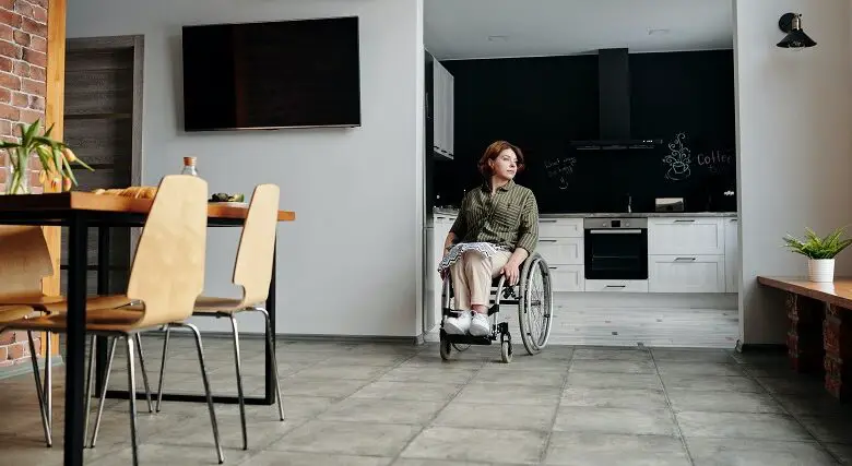 Woman using a wheelchair wheeling out from her open-plan kitchen into her dining room