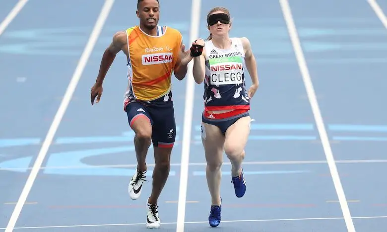 Libby Clegg in Team GB kit, wearing a blindfold and with her running guide