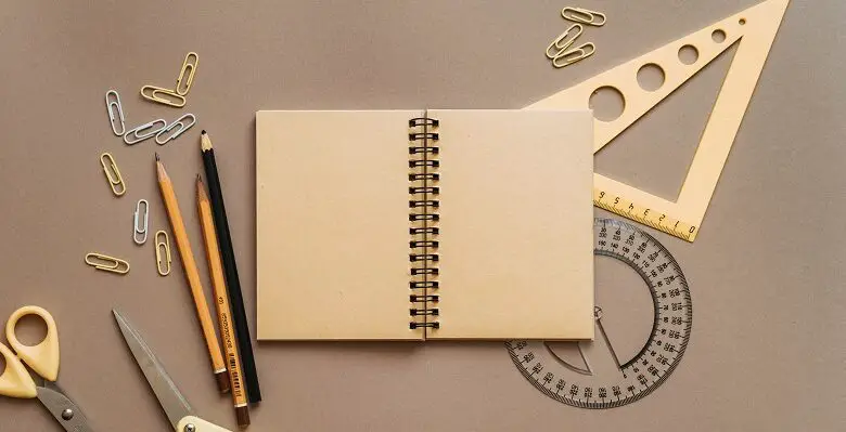 A notepad, pencils, paper clips and rulers on a brown background