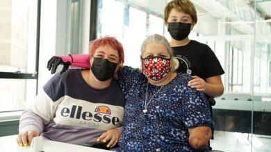 Susan Neil in her wheelchair with a pink Open Bionics prosthetic arm and her two children all wearing face masks