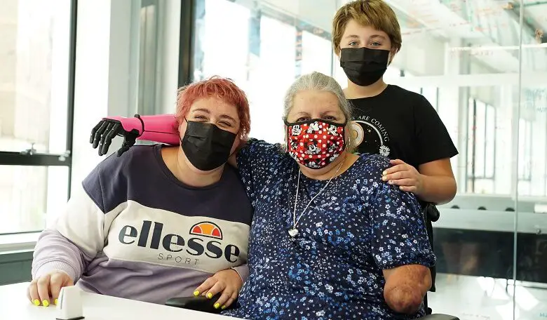 Susan Neil in her wheelchair with a pink Open Bionics prosthetic arm and her two children all wearing face masks