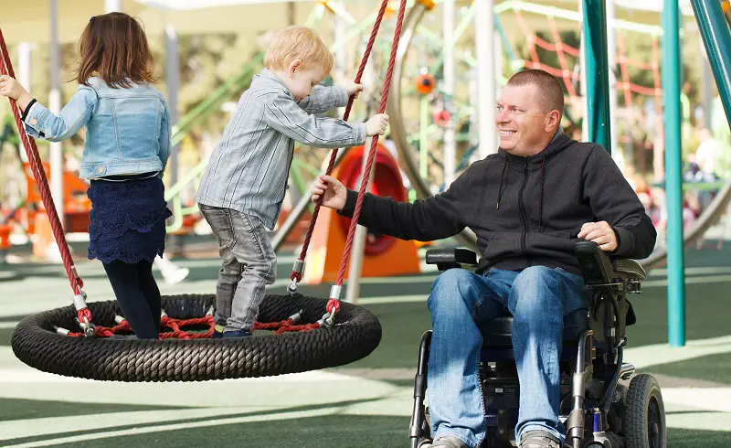 A man in a wheelchair with two children in a playground