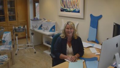 Chris Buckingham in her office with Glideboard transfer boards, the walking frame caddy, Easywipe bottom wiper and BraBuddy dressing aid behind her