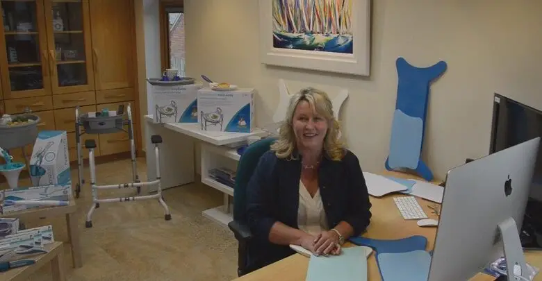Chris Buckingham in her office with Glideboard transfer boards, the walking frame caddy, Easywipe bottom wiper and BraBuddy dressing aid behind her