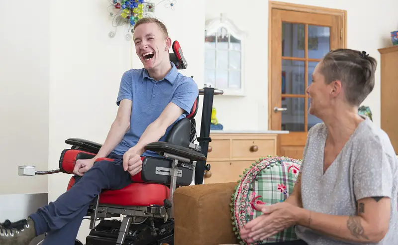 Disabled man in a wheelchair laughing with a woman sat in a red sofa
