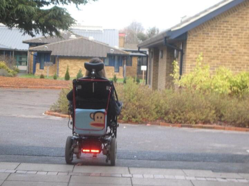 Emma Purcell in her powered wheelchair with hwr back facing the camera walking around the school grounds