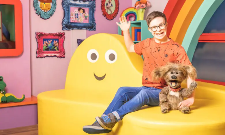 George Webster in CBeebies studio wearing orange T-shirt, blue jeans and glasses