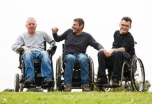 Three men in wheelchairs in a field laughing with each other