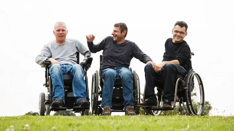 Three men in wheelchairs in a field laughing with each other