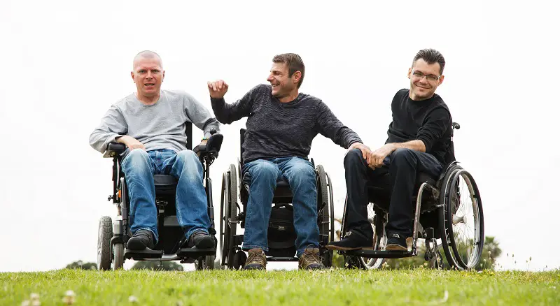 Three men in wheelchairs in a field laughing with each other