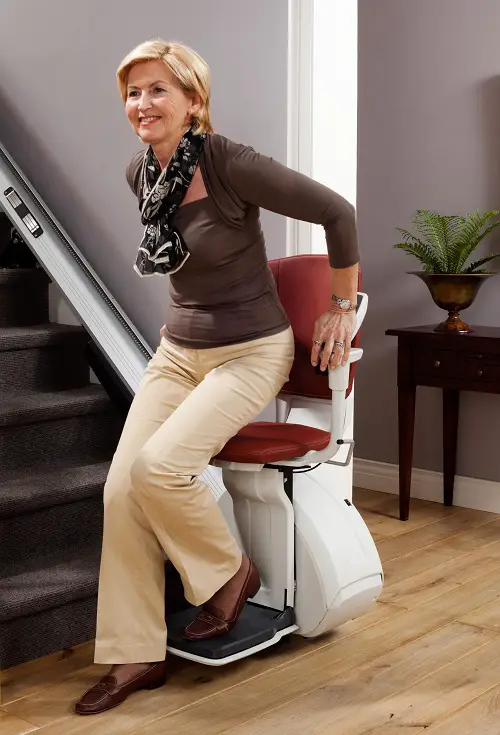 An older lady getting up from a stairlift in a hallway
