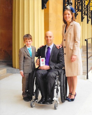 Rob Smith in suit holding MBE award