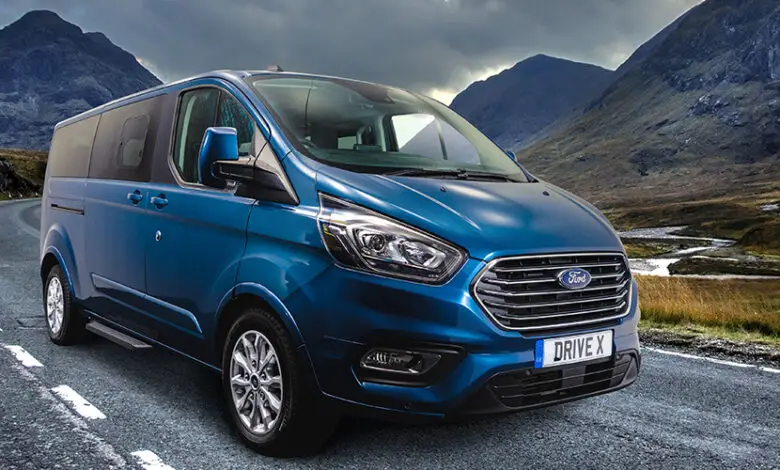 Blue Ford Drive X wheelchair accessible vehicle from Sirus driving along a road with mountains in the background