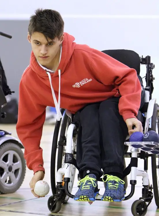 Louis Saunders in his wheelchair wearing a red hoodie playing boccia
