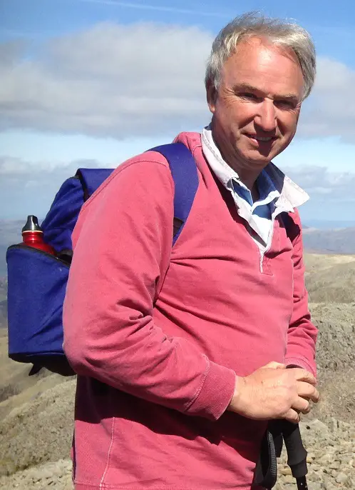 Richard Pertwee, founder of The Challenge Hub, wearing a pink shirt and a blue backpack walking over mountains